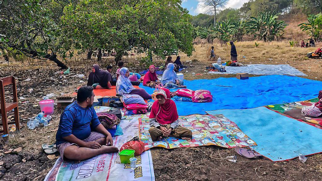 A group of people sit outdoors on blankets and tarps