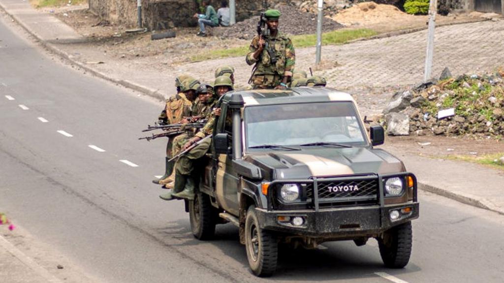 A military jeep drives down a road with armed soldiers gathered in the back.