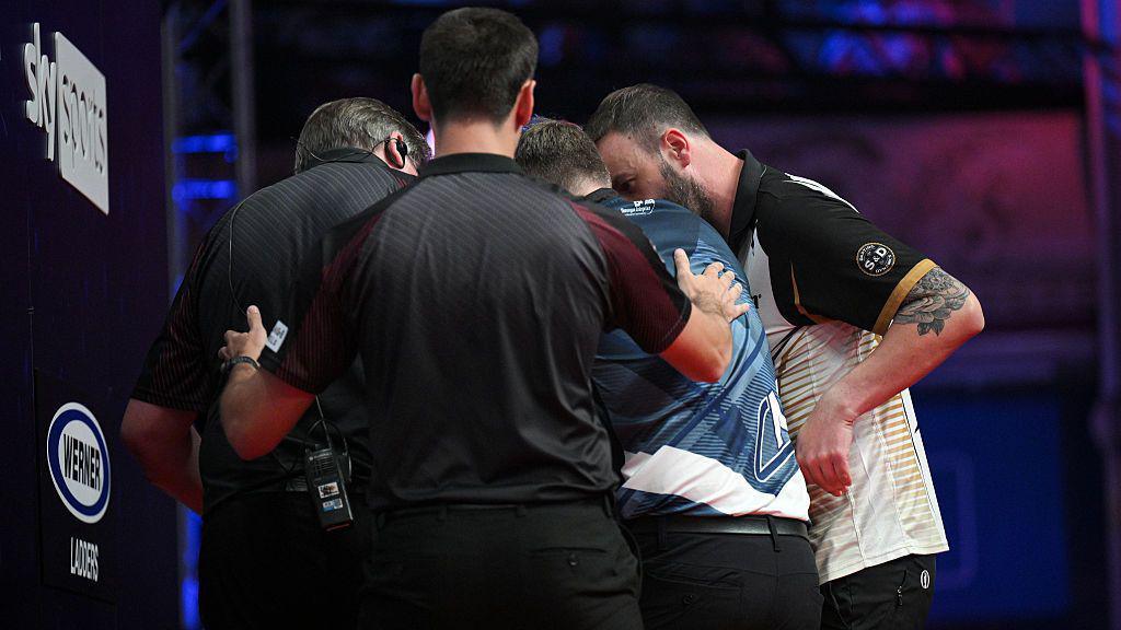Ross Smith and officials hold up Cameron Menzies on stage at a darts game