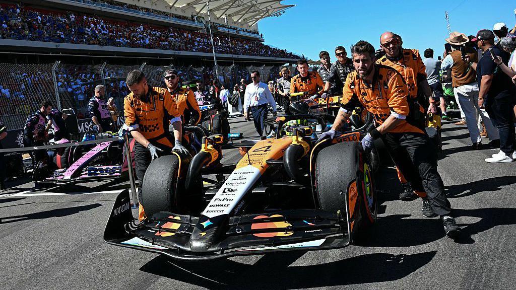 McLaren mechanics push Lando Norris' car onto the track