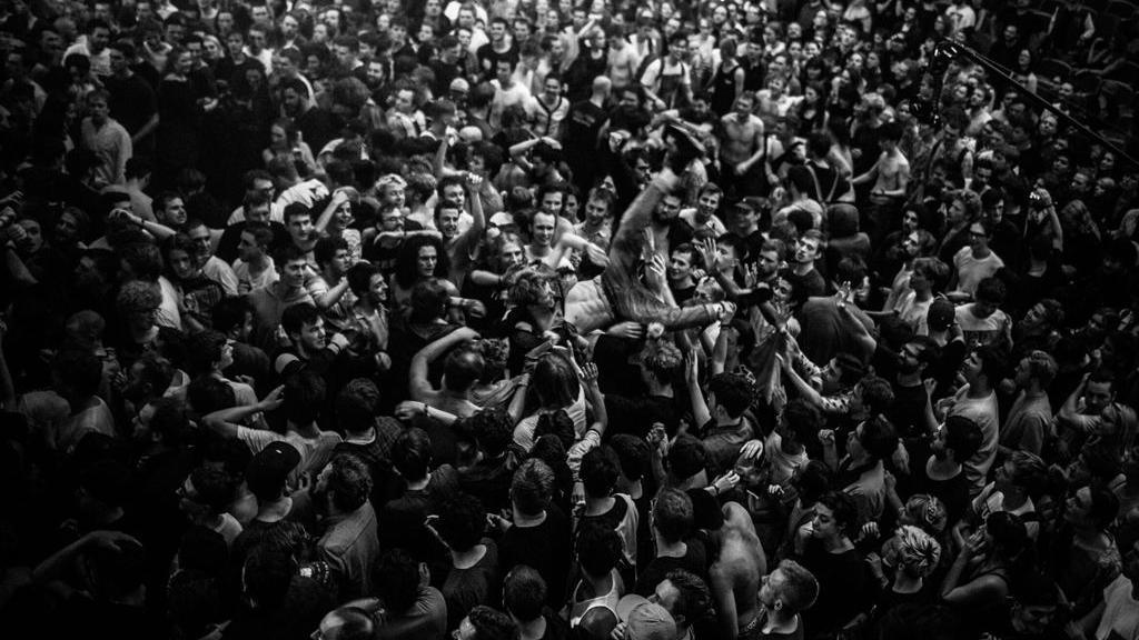 Black and white image of someone crowdsurfing at Simple Things while Death Grips perform (who you cannot see)