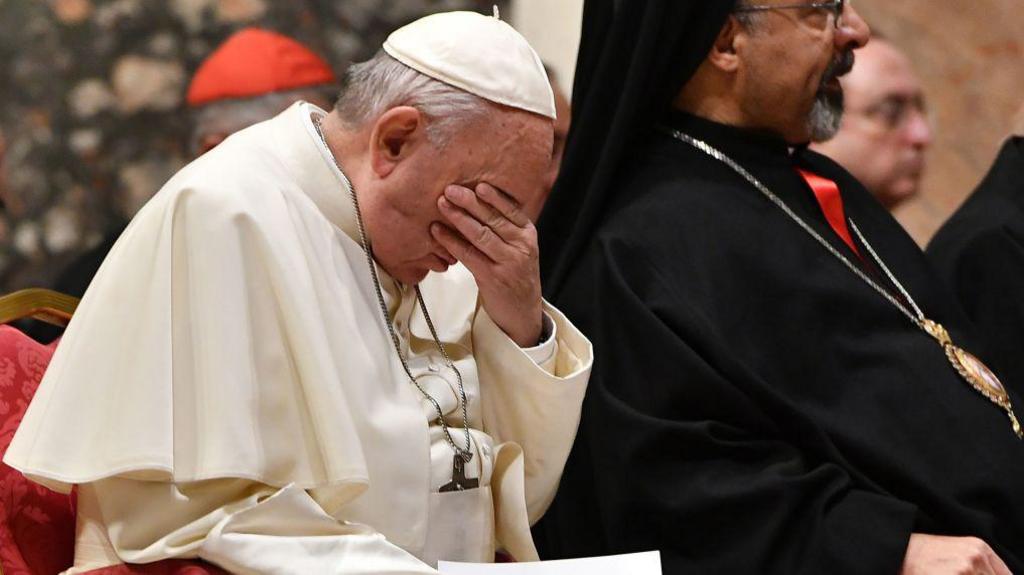 Pope Francis holds his head in his hands during a prayer