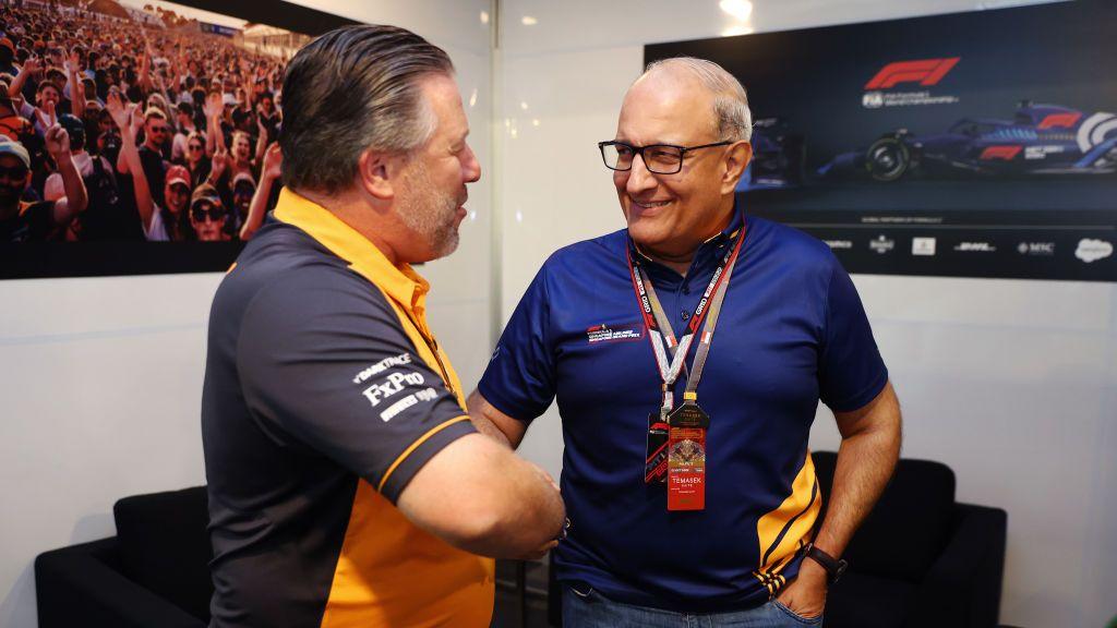 Subramaniam Iswaran shakes hands with McLaren Chief Executive Officer Zak Brown in front of televisions showing Formula 1