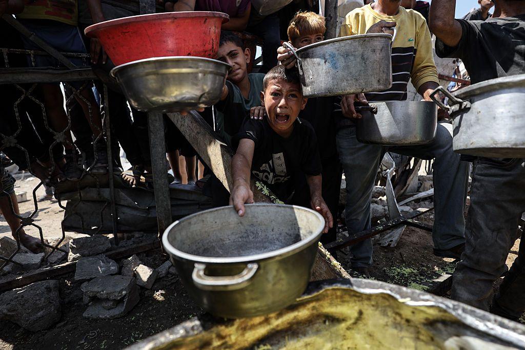 A child wails as he and others hold empty pans towards the camera