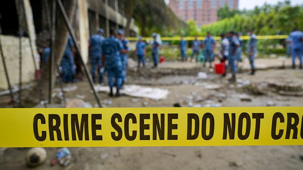 A crime scene barrier tape cordons off the area as Bangladesh Air Force personnel inspect the crash site a day after a training jet crashed into a school in Dhaka
