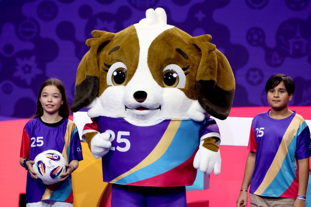 Two children standing next to Euro 2025 Mascot Maddli.