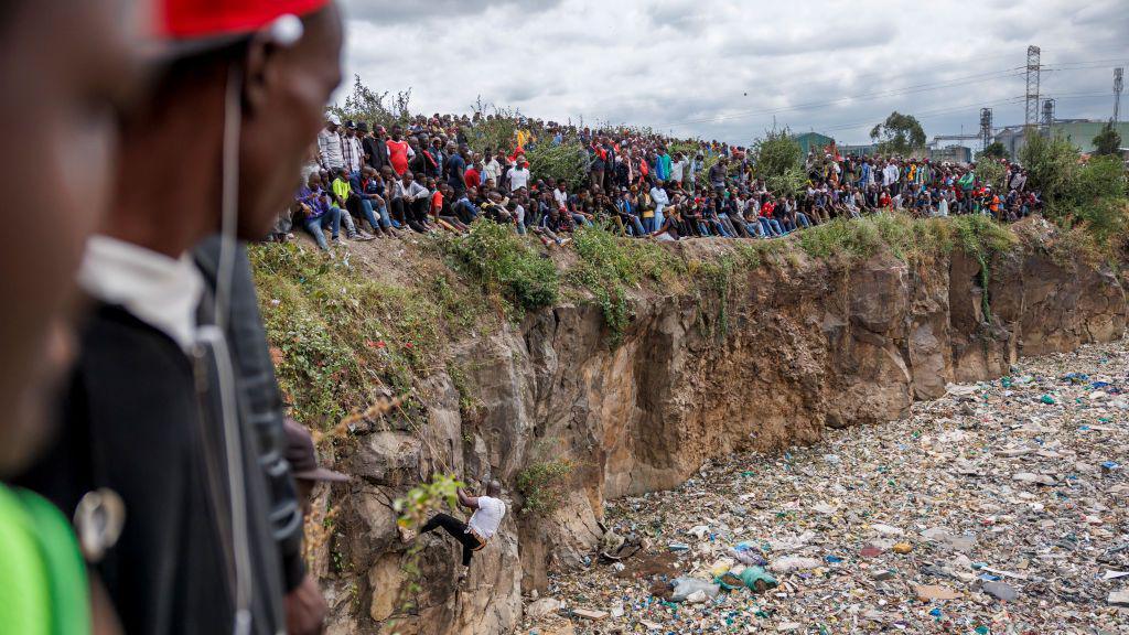 Crowds gather on the edge of an abandoned quarry to watch volunteers searching through a rubbish dump for human remains at Mukuru slum in Nairobi on July 14, 2024