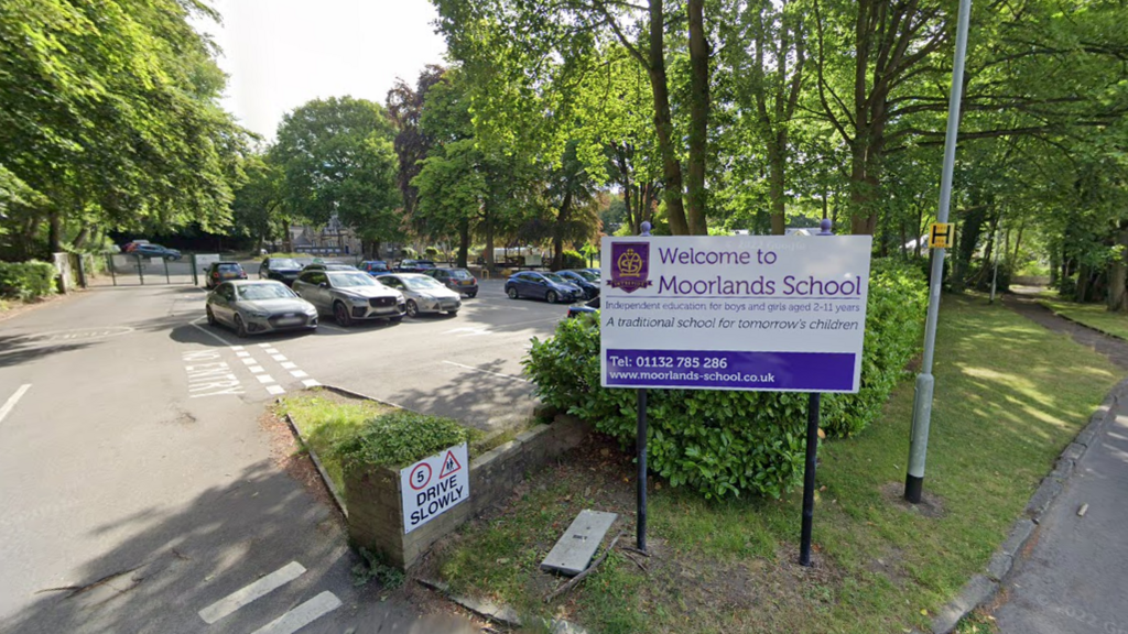 A white and purple sign outside a car park that reads: Welcome to Moorlands School