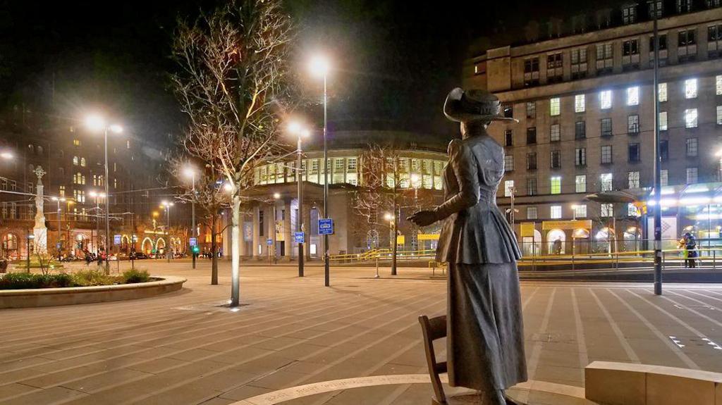 St Peter's Square at night with the statue of Emmeline Pankhurst in the foreground with the tram stop, town hall annexe and 