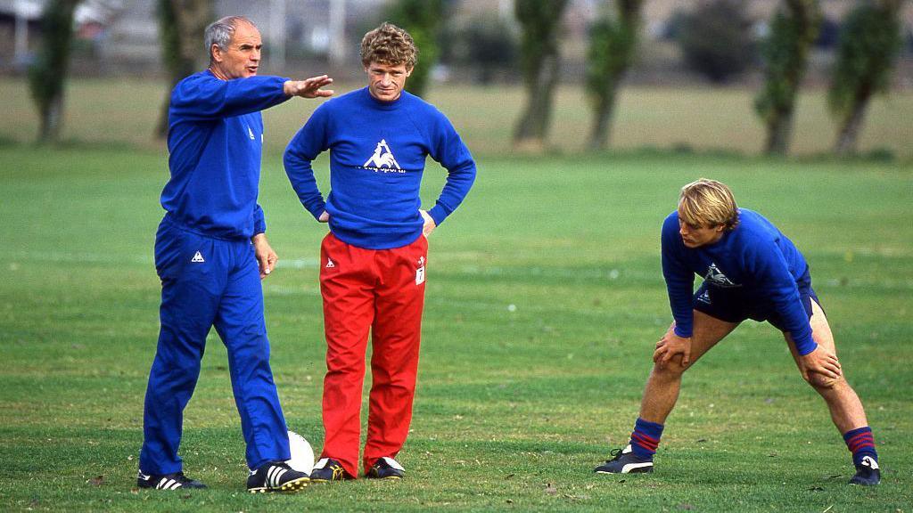 Ernie'n hyfforddwr gyda Chelsea yn 1985 ac yn rhoi cyngor i'r chwaraewyr  Micky Hazard a John Bumstead