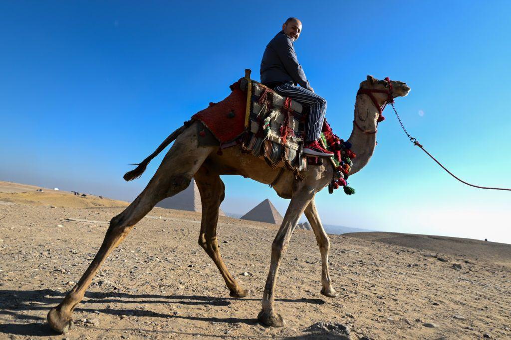 A tourist on a camel in Giza, Egypt with the backdrop of the pyramids.