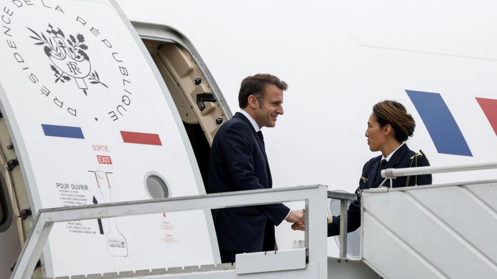 French President Emmanuel Macron stepping off plane in Mayotte, greeted by a woman 