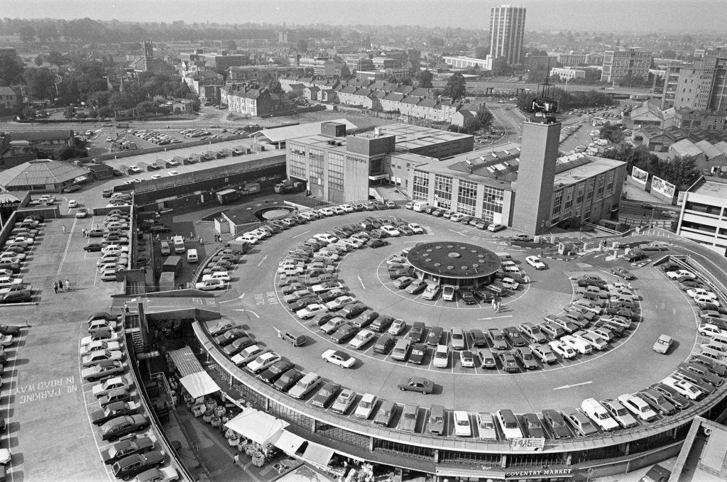 A black and white aerial image of Coventry Market's circular rooftop car park, with dozens of vehicles parked on it. Other city centre buildings can be seen in the background