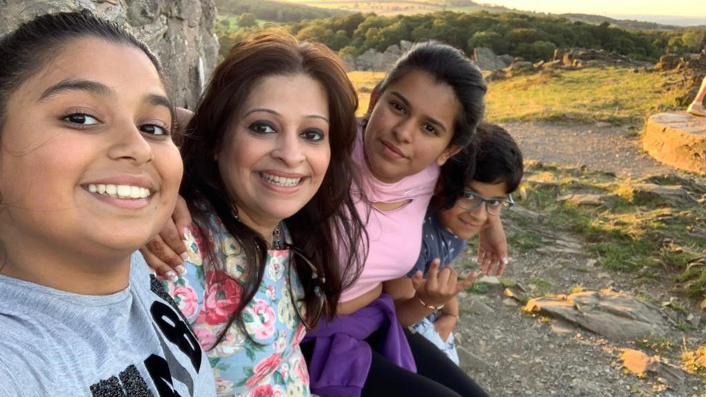 Leela Keshavji - second on the left - with her three children. They are all stood with their arms around each other outside.