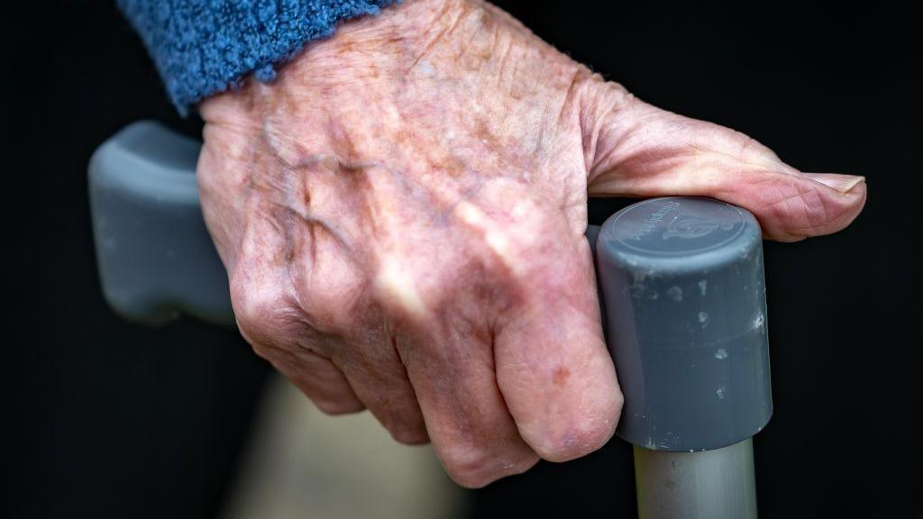 A stock image of an elderly person holding a crutch. 