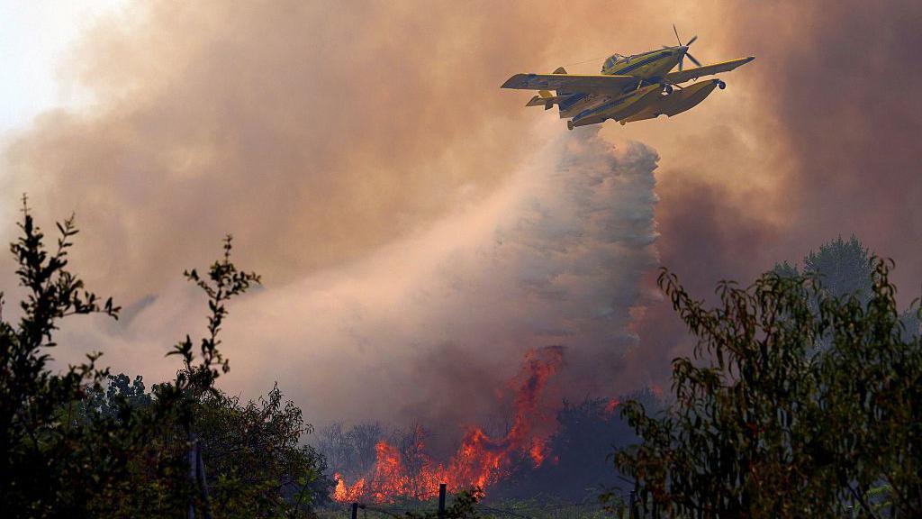 Plane dumps water on wildfire - scene filled with smoke and flames. 