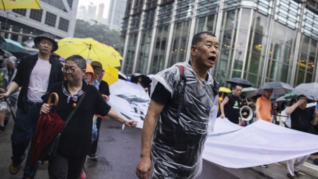 Jimmy Lai stands in the middle of a protest wearing a plastic raincoat
