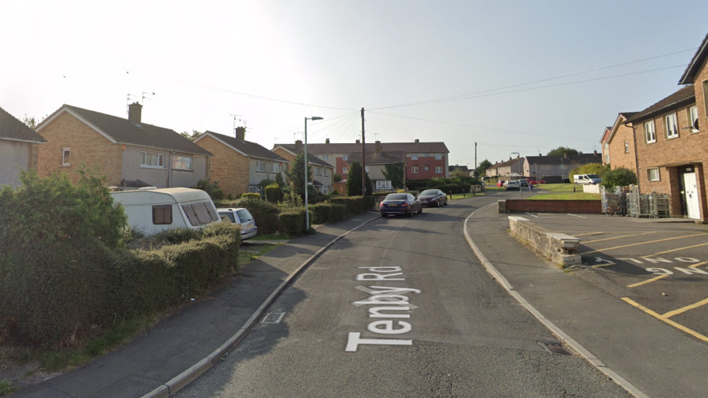 A Google Streetview of Tenby Road. There is a small carpark/loading bay on the right of the picture, and houses with driveways to the left.