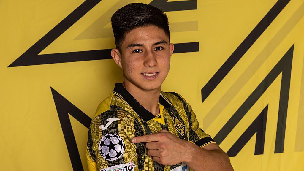 Dastan Satpaev of Kairat Almaty pointing to the Champions League logo on the arm of his shirt