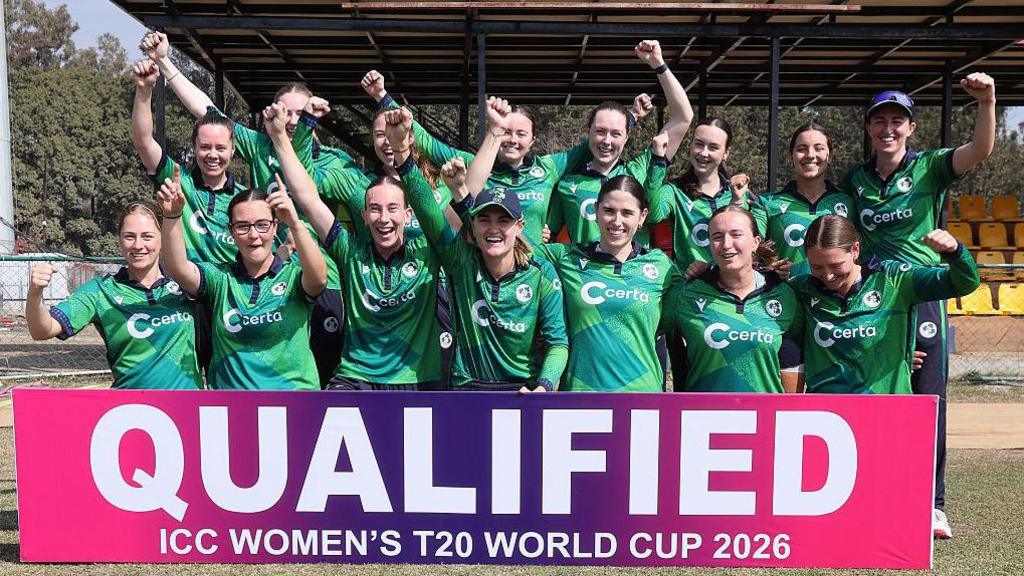 Ireland players celebrate in front of a sign that reads 'qualified: ICC Women's T20 World Cup 2026'