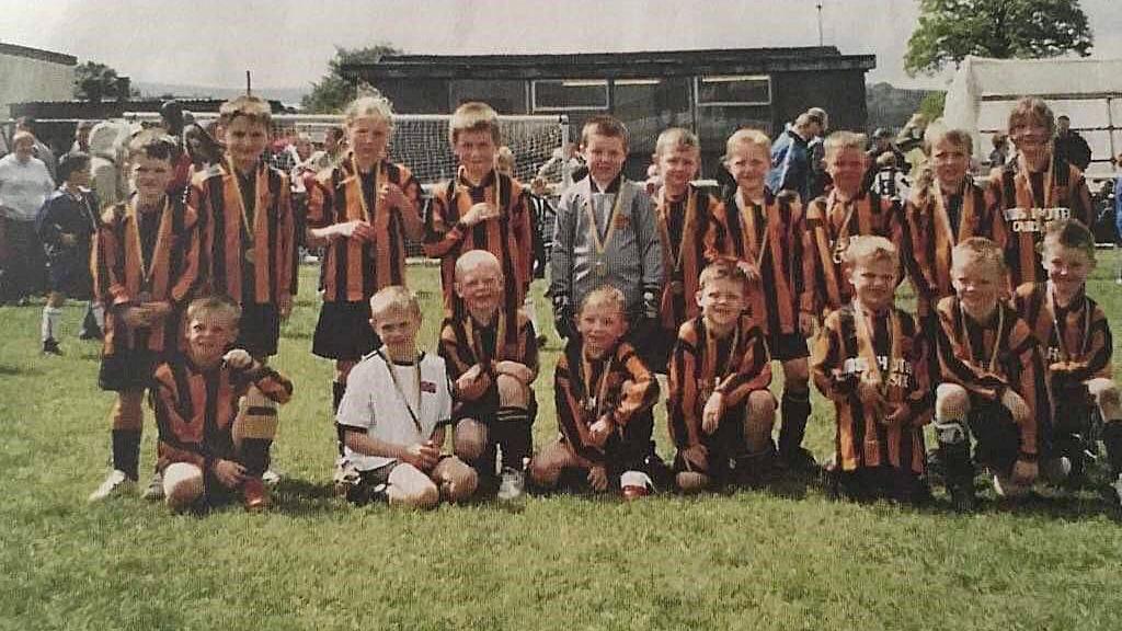 A team of young footballers in yellow and black strips line up for a team picture on the grass with medals around their necks