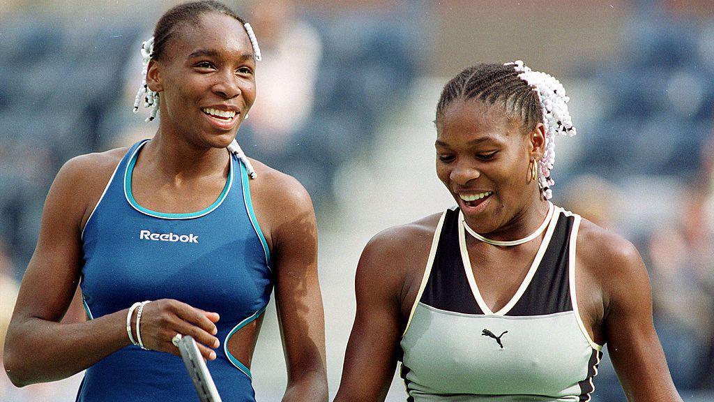 Sisters Venus Williams and Serena Williams smiling and chatting to each other on court.