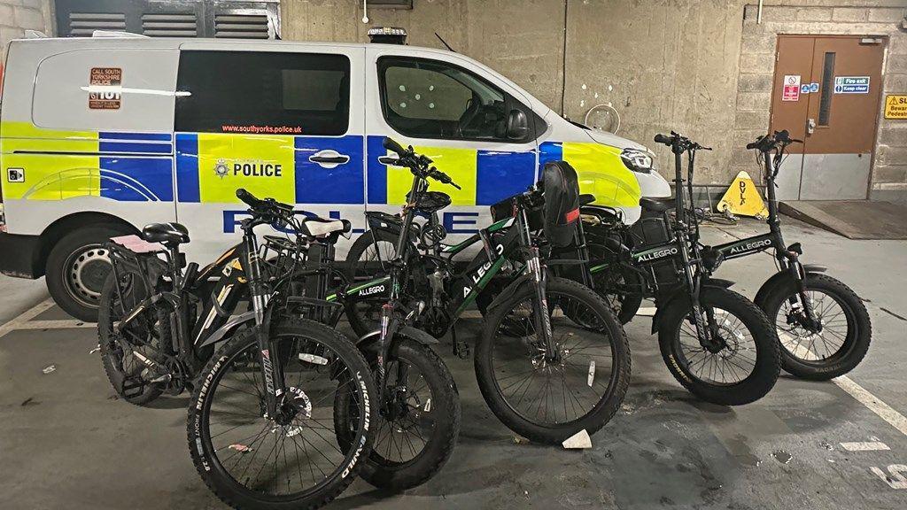 Five electric bikes in front of a police van in an underground car park.