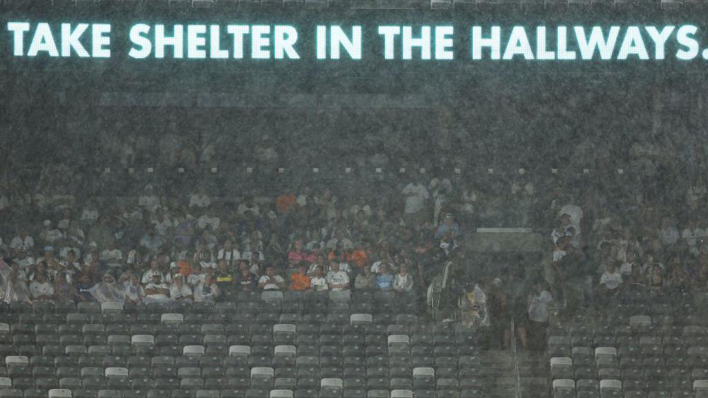 Fans take shelter from the rain during the friendly between Barcelona and Real Madrid