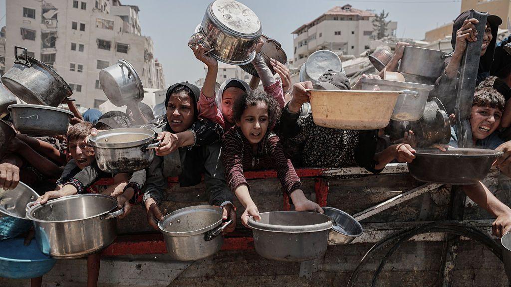 Palestinians, including children, wait in line to receive hot meals distributed by the charity organisation in Gaza City, Gaza on 30 July 2025