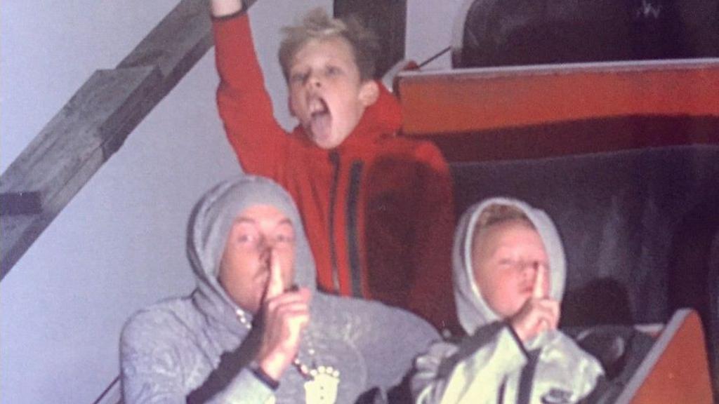 Richard and his two young sons riding Megafobia rollercoaster. Richard is sitting in a row with one of his boys, and both are wearing hoodies and putting their fingers to their mouths. In the row behind his other son has one arm in the air with his mouth open wide.