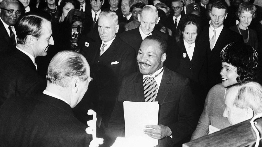 Black and white photograph, in it Martin Luther King Jr, shakes Crown Prince Harald and King Olav's hand in 1964 after winning the Nobel Peace Prize.