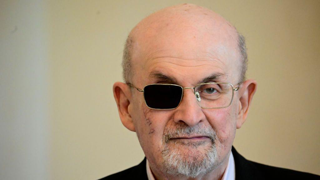 Sir Salman Rushdie pictured. He is wearing glasses, with one side darkened because he was blinded.