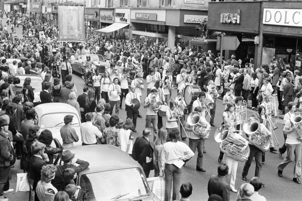 A brass band is leading a parade through Birmingham city centre during the production of the 1973 film.