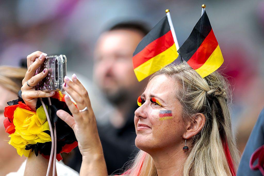 A German fan takes a picture with her phone. She is wearing eyelashes in the colours of the German flag and two small flags tucked into her hair