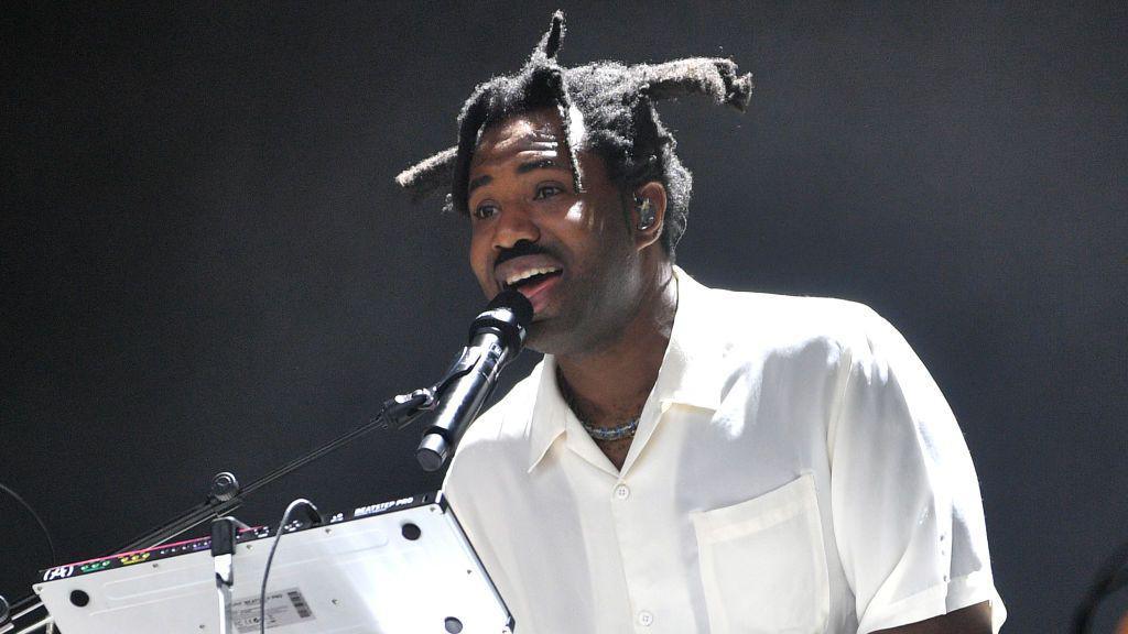 Sampha performing on stage wearing a white shirt.