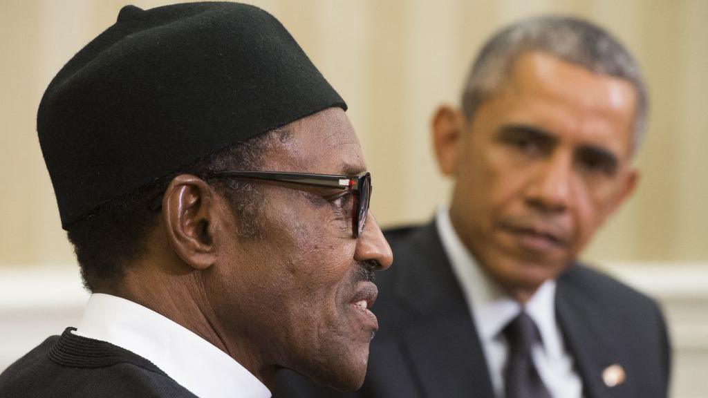 Barack Obama is pictured, out of focus, looking at Buhari, who is speaking and staring straight ahead.