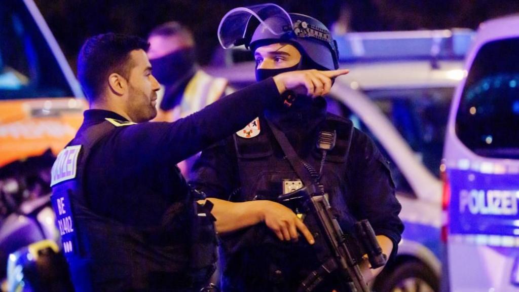A police officer carrying a machine gun (R) and a colleague talk near the scene where several people were injured 