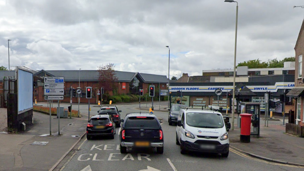 The approach to a signal-controlled crossroads with cars queueing and a line of traffic exiting towards the camera