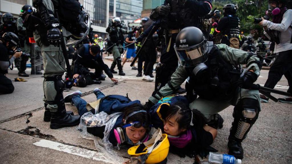 Riot police pin down two female protesters during an anti-China protest in September 2019