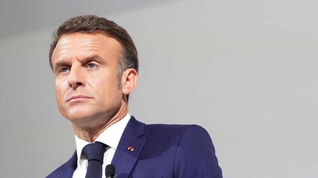 French President Emmanuel Macron wearing a blue suit with a stern look on his face