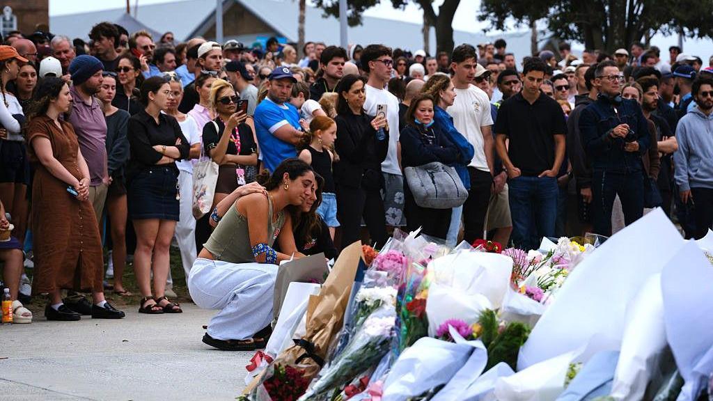 Women lay flowers in front of crowds at a vigil for Bondi beach victims