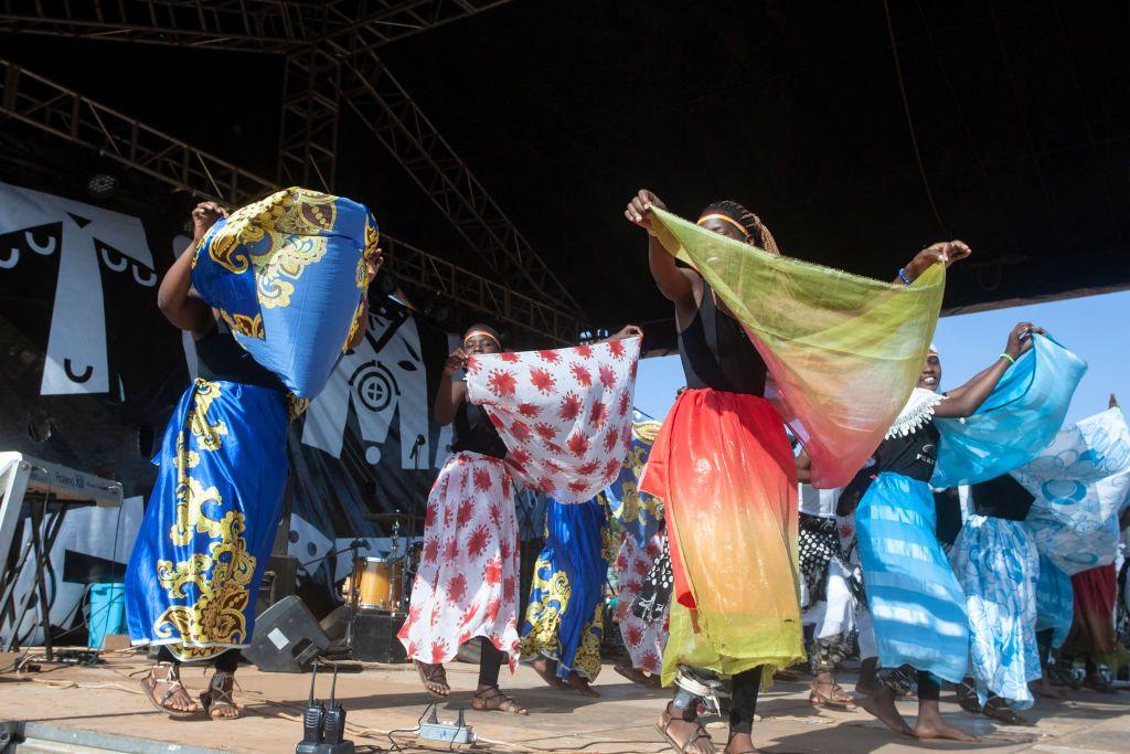 A group of female refugees perform on stage, holding up material that matches their skirts as part of a  traditional cultural dance at the Dzaleka Refugee Camp in Dowa, Malawi - Saturday 2 November 2024