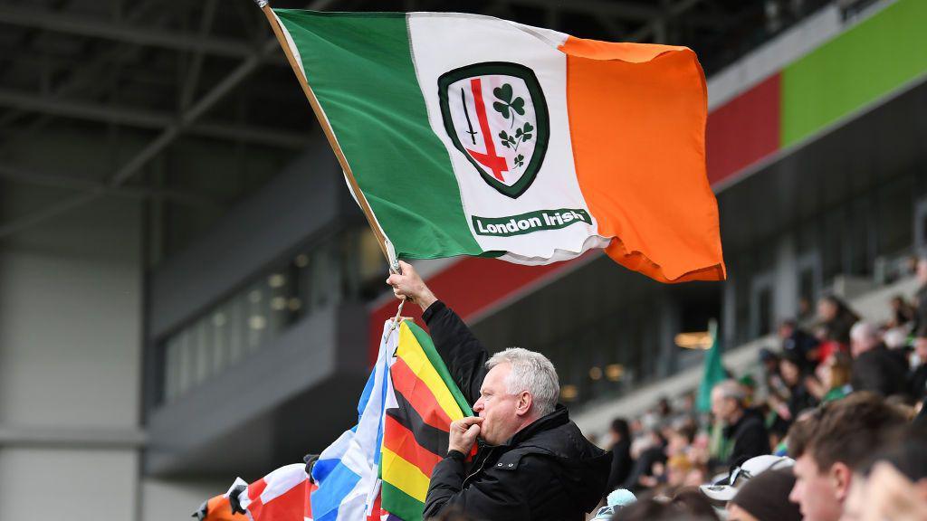 A crowd shot with a fan waving a London Irish flag