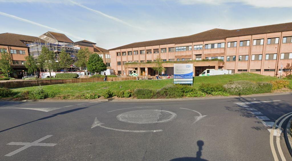 A red brick building, with two ambulances outside and a sign that says Musgrove Park Hospital. In the foreground is a mini roundabout. 