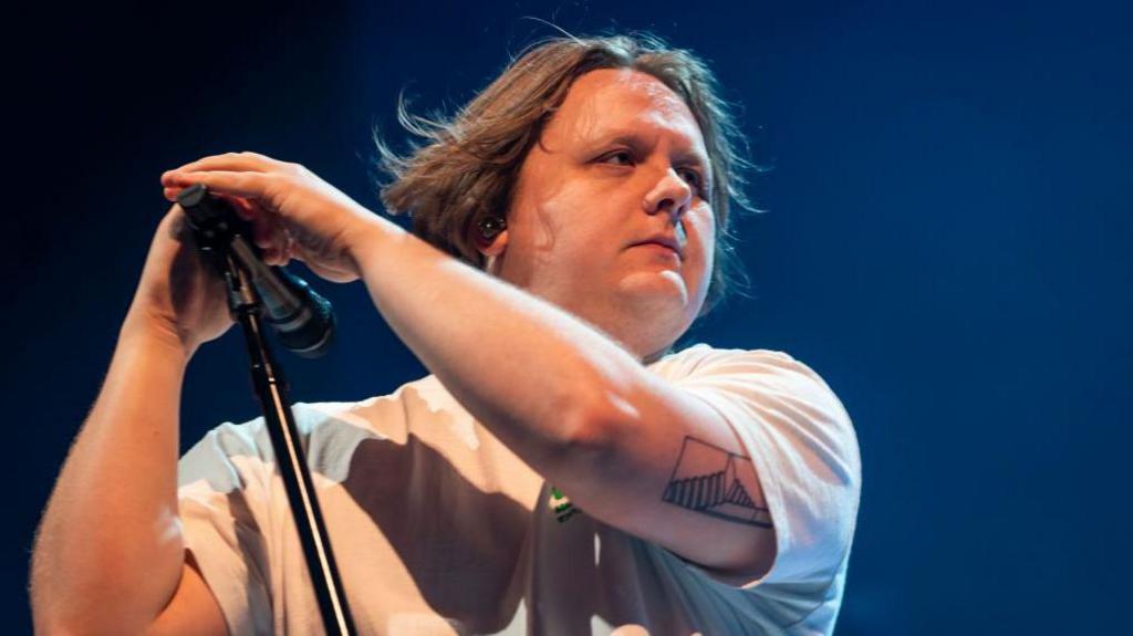 A photo of Lewis Capaldi on stage holding a microphone stand