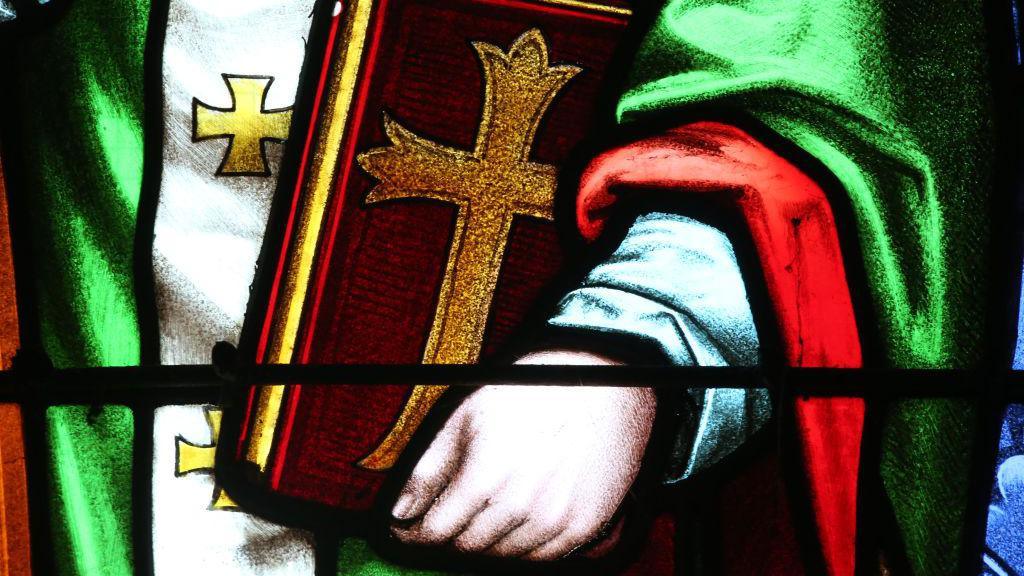 A stained glass window depicting St Augustine of Hippo holding a bible.