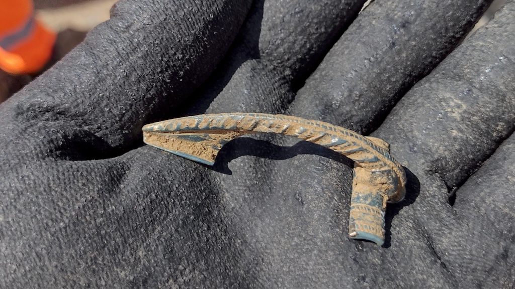 A gloved hand holding a Roman artefact found in the A417 excavation.