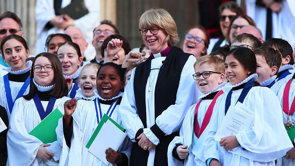 dame sarah mullally and children in religious clothing.