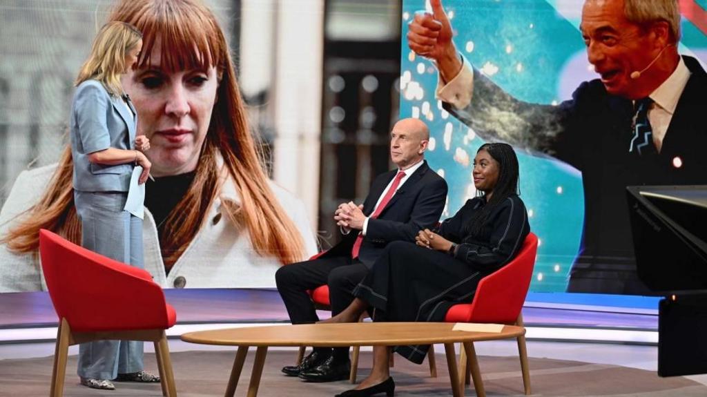 John Healey and Kemi Badenoch sit in the BBC studios in front of Laura Kuenssberg. 