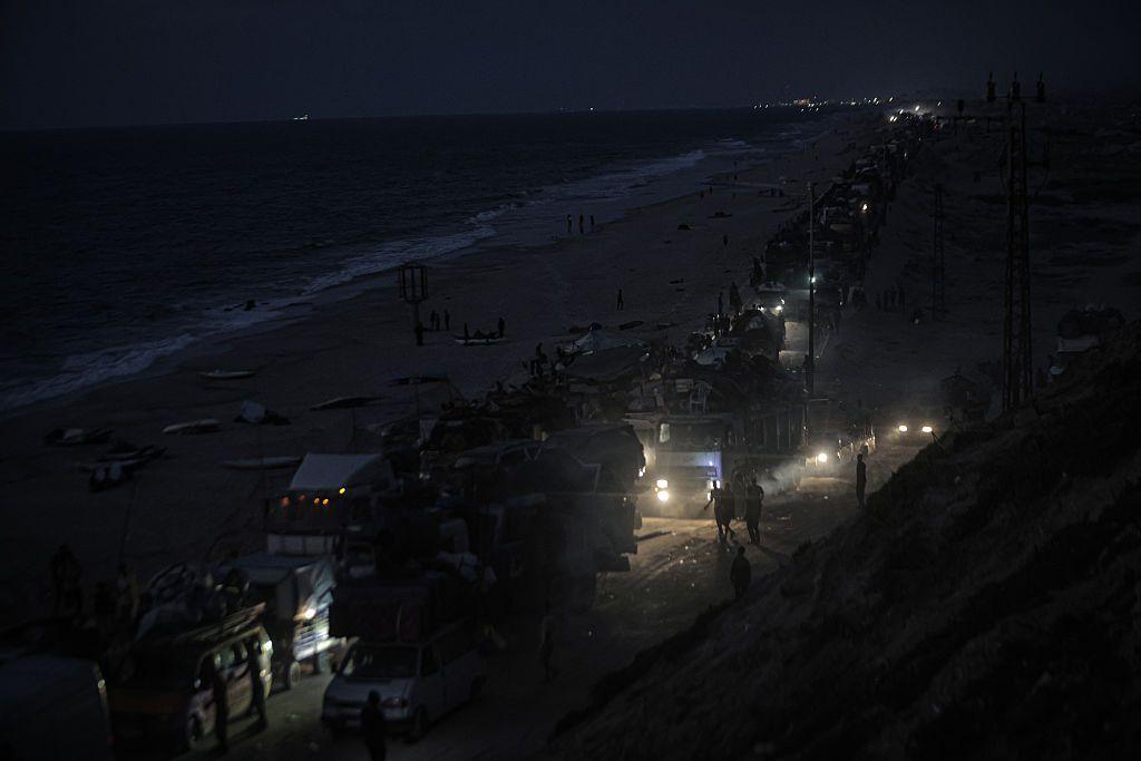 At night, in the dark, a stream of cars slowly moves down a coastal road. 